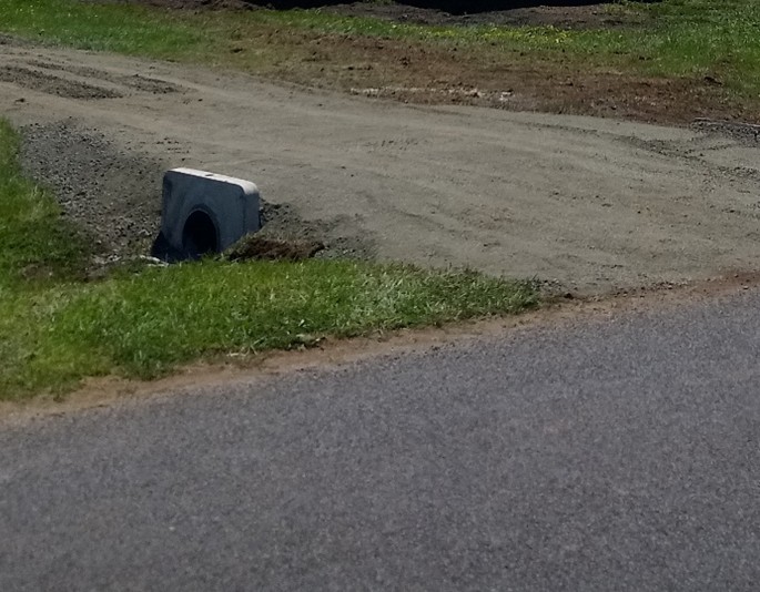 An image of an unsealed driveway crossing over a concrete pipe.